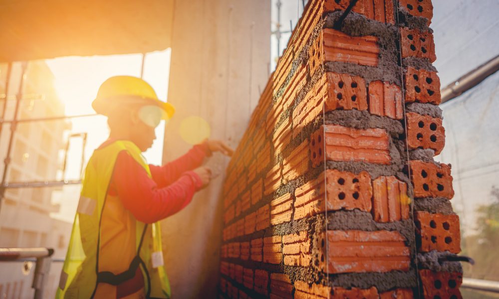 Bricklayer construction worker installing red brick masonry on exterior wall at outdoors construction site